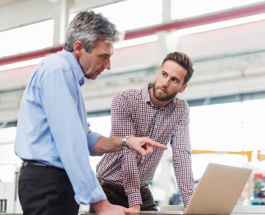 two men discussing and standing behind a laptop